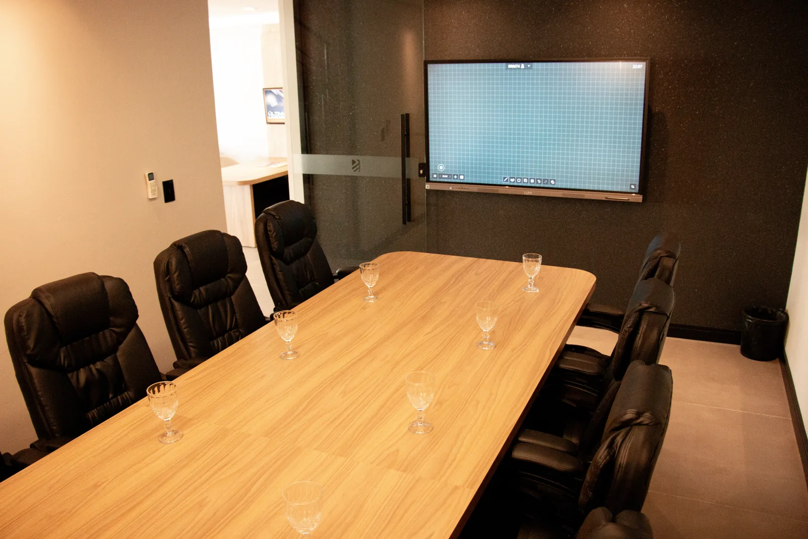 Sala de reunião com mesa de madeira e tela digital para apresentações.