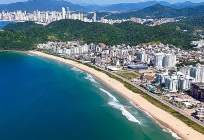 Vista aérea de uma orla do litoral norte de Santa Catarina, com a praia entre o mar e os prédios